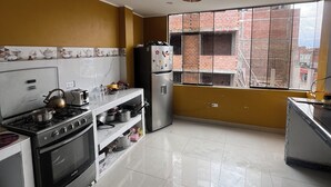 Uma cozinha com fogão a gás, forno, geladeira e uma janela com vista para um prédio de tijolos.