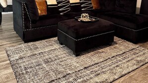 A modern living room with a black sectional sofa, ottomans, and a patterned rug. - Modern Executive Suite- NRG, Medical Center, Downtown Houston (Houston)