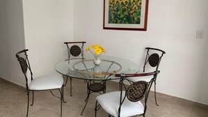 Un comedor con una mesa de vidrio rodeada de sillas de mimbre y un jarrón con flores amarillas.