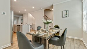 A dining area with a wooden table set for four, surrounded by modern chairs. A vase with white flowers is on the table.