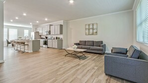A spacious living area with a grey sofa, a coffee table, and a kitchen in the background.
