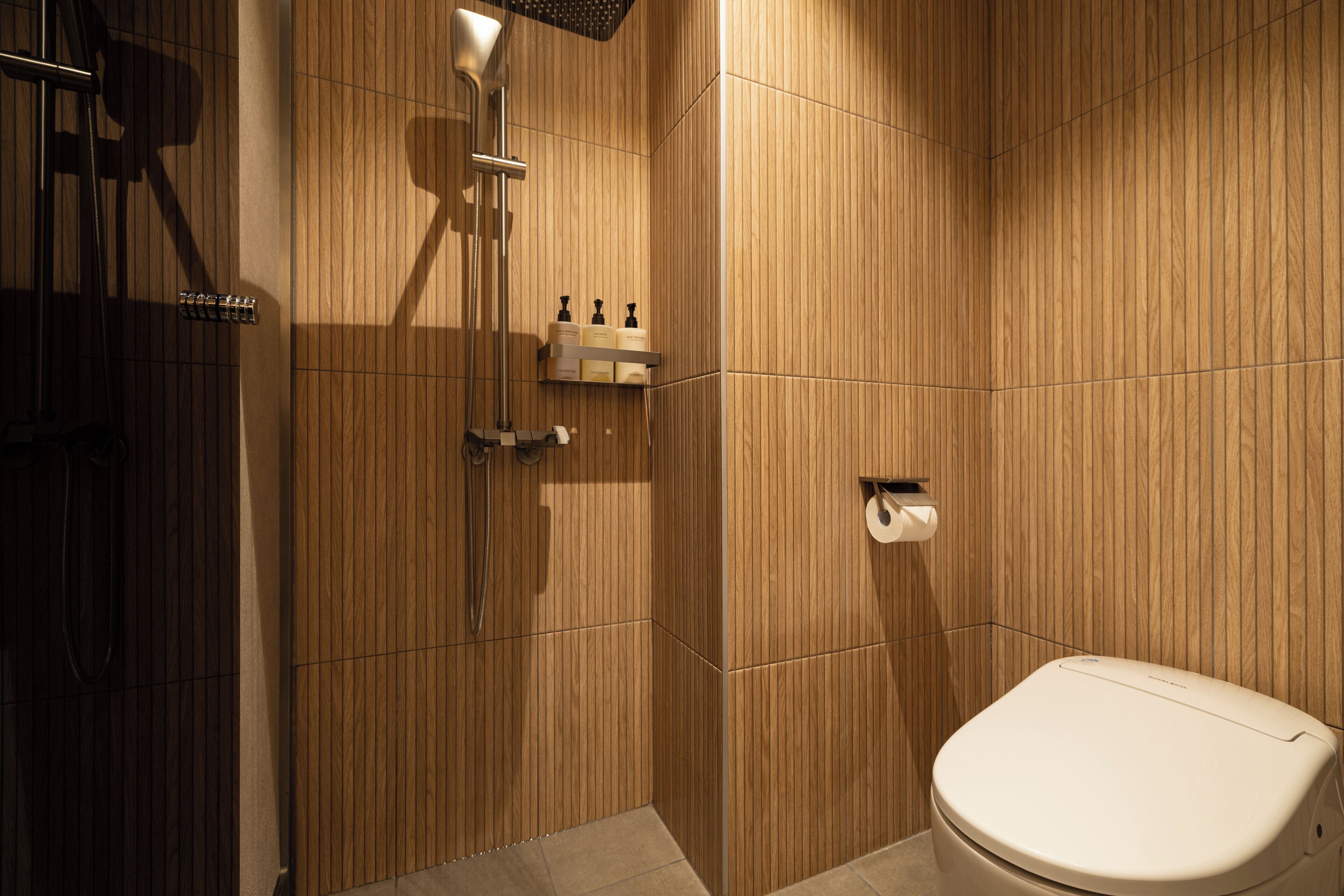 Une salle de bain moderne avec un lambris en bois, une douche, des toilettes et une étagère contenant des articles de toilette.