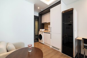 Un espacio habitable compacto con sofá, una mesa redonda con un vaso, lavadora y horno empotrado.