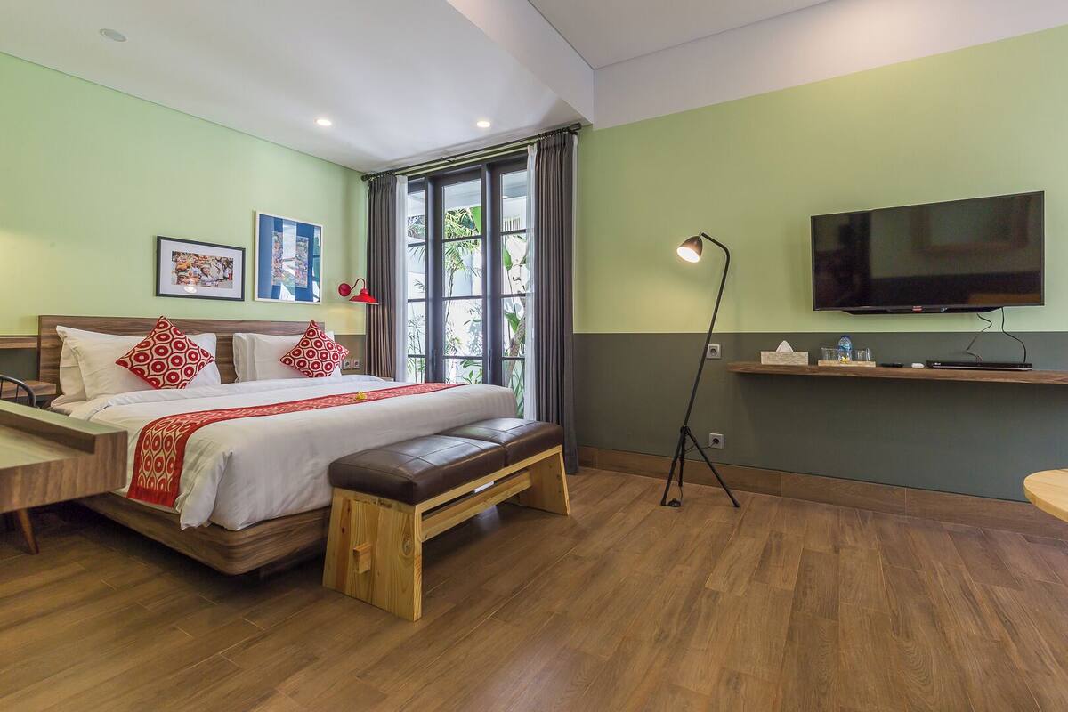 A modern hotel room with a large bed, a bench, a desk, a TV, and a window with curtains.