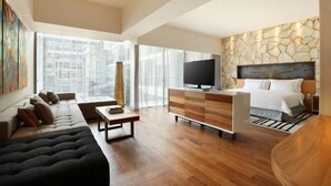 Une chambre d’hôtel moderne avec un grand lit, une télévision, une commode en bois, un canapé et une table à manger.