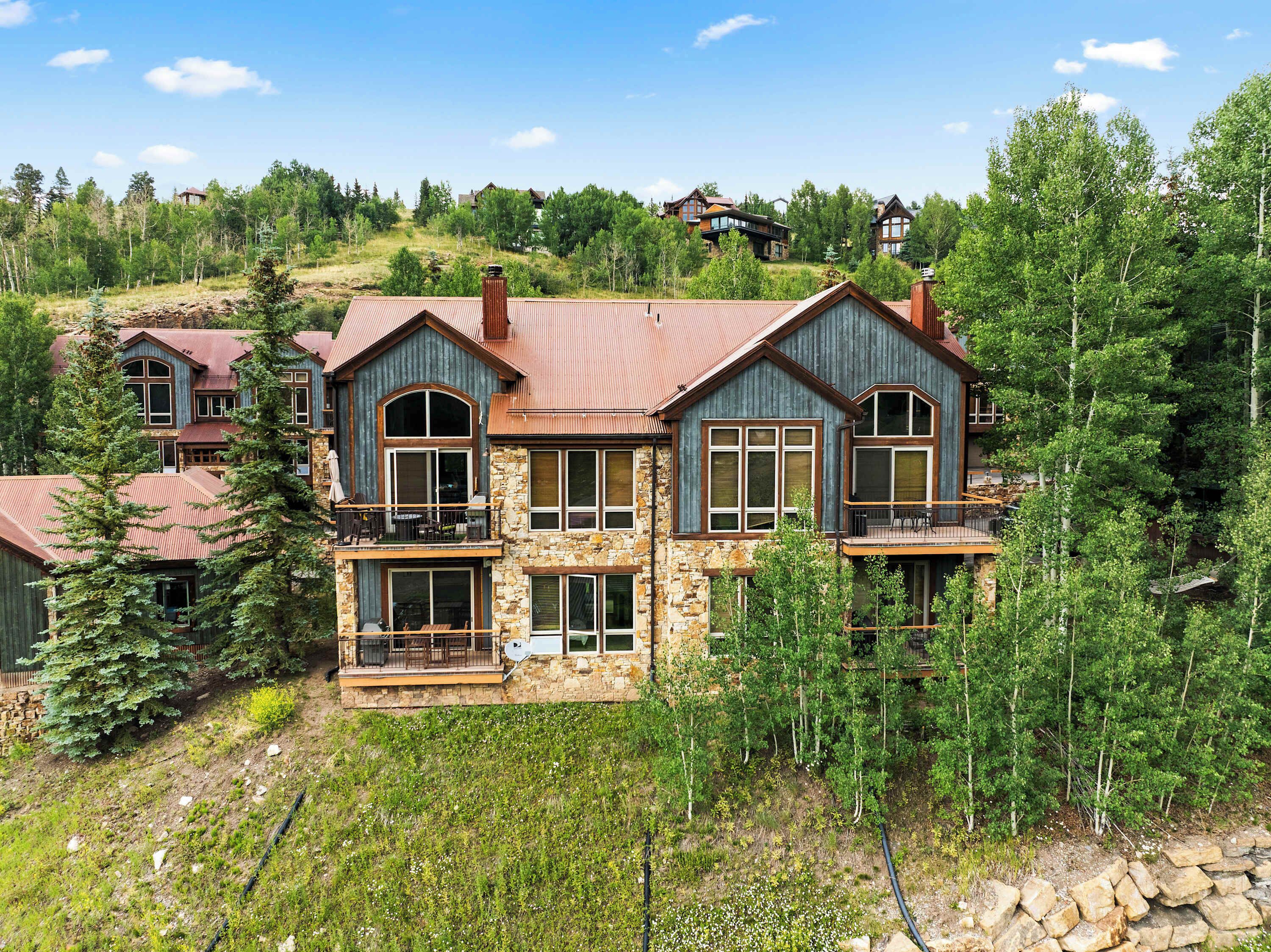 A large, multi-story house with stone and wood exterior, multiple balconies, and large windows.