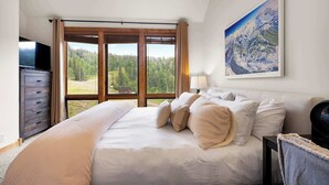 Quarto com cama grande, penteadeira, televisão e pintura de paisagem de montanha.