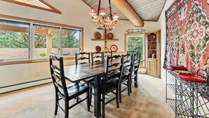 Comedor con mesa y sillas de madera, una araña y vistas a zonas verdes.