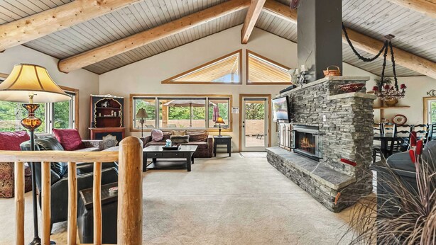 Un salón espacioso con chimenea de piedra, vigas de madera y ventanas amplias.