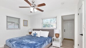 Une chambre à coucher comprenant un lit, un ventilateur de plafond, des lampes de chevet et une porte donnant sur une autre pièce.