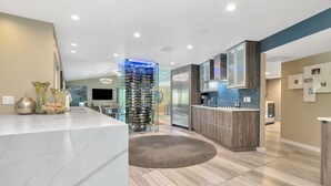 A modern kitchen with a marble countertop, a central island, and a built-in wine rack. - Papys Preserve | Luxury Waterfront Estate w/ Pool (St Petersburg)