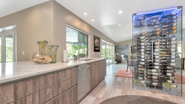 A modern kitchen with a wine rack, wooden cabinets, and a large window. - Papys Preserve | Luxury Waterfront Estate w/ Pool (St Petersburg)