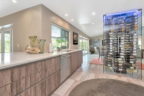 A modern kitchen with a wine rack, wooden cabinets, and a large window. - Papys Preserve | Luxury Waterfront Estate w/ Pool (St Petersburg)