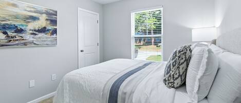 A bedroom with a bed, a painting, a door, and a window.