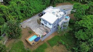Un edificio de dos plantas con piscina en la azotea, rodeado de abundante vegetación.