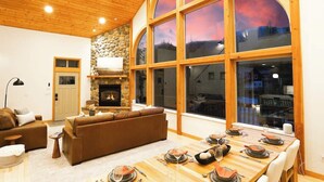 A spacious living room with a fireplace, a dining area with a table set for four, and large arched windows.