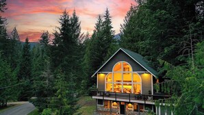 A cabin with a large window, a deck, and surrounded by trees.