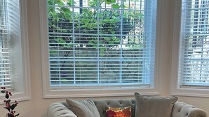 A living room with a beige sofa, a woven chair, and a window with blinds.