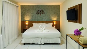 Een hotelkamer met een groot bed, een flatscreen televisie aan de muur, een houten hoofdeinde en een wandlamp.