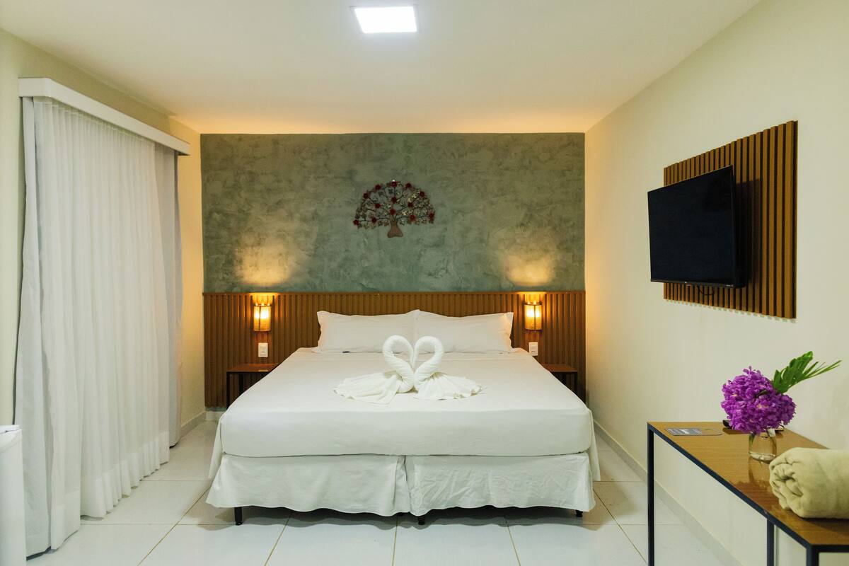 Habitación de hotel con una cama grande, un televisor de pantalla plana montado en la pared, un cabecero de madera y una lámpara de pared.