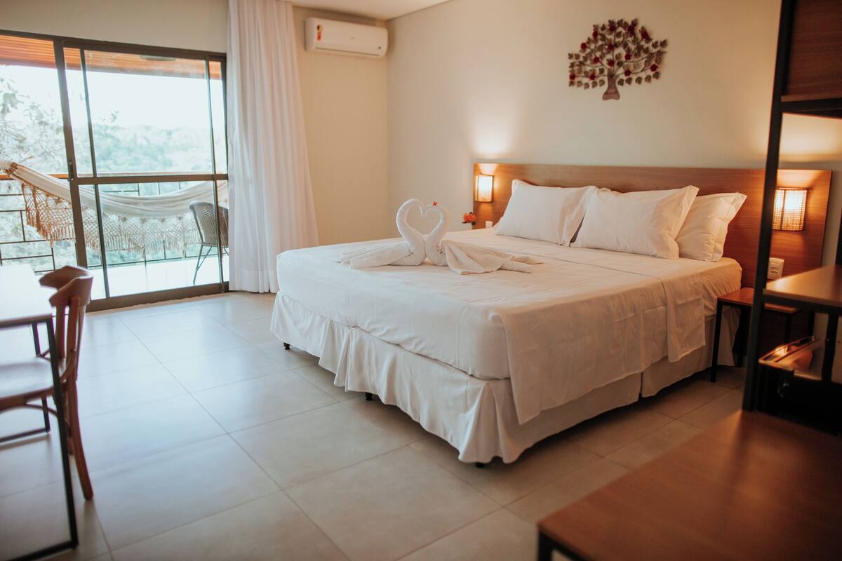 Una habitación de hotel con una cama grande, un balcón con una silla y un aire acondicionado de pared.