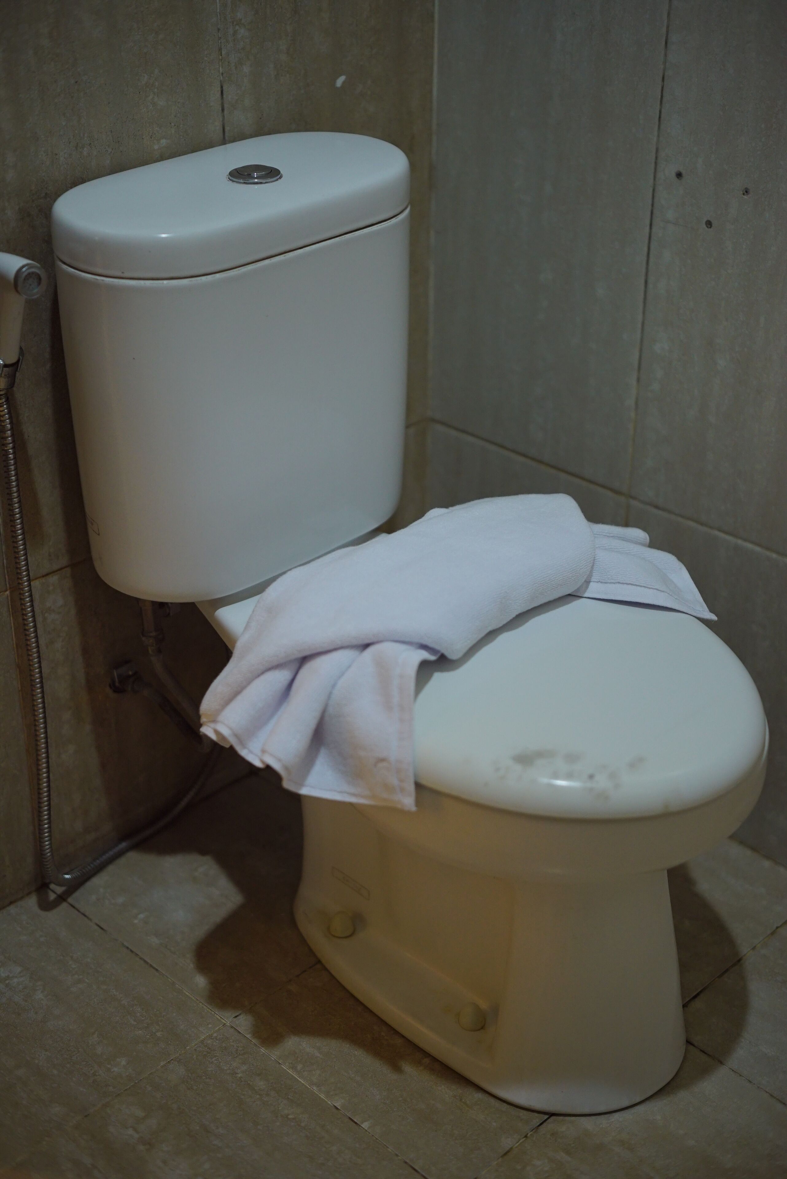 Inodoro blanco con una toalla sobre el asiento en un baño con paredes y suelo de baldosas.
