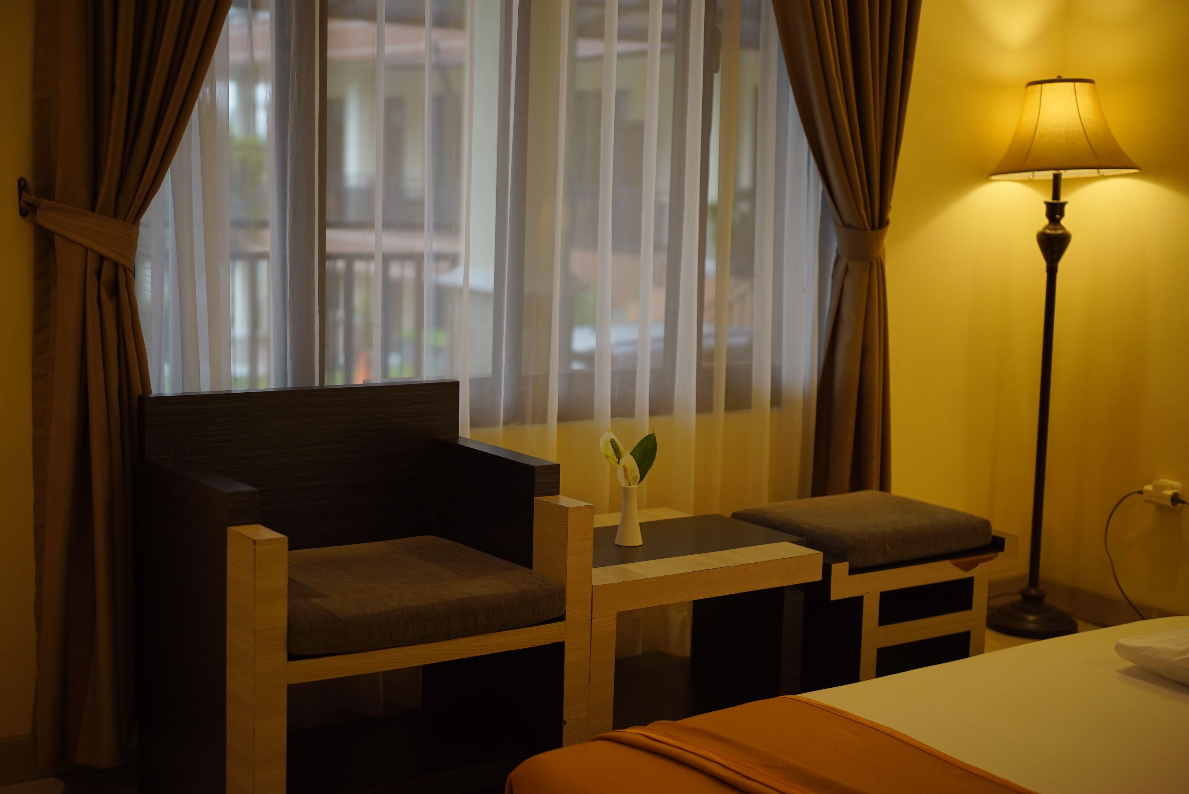 A hotel room with a bed, a desk with a chair, a lamp, and a window with curtains.