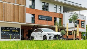 A modern building with a sign for Tenis Resort Sihk & Hotel Breas. A white Lexus RX is parked in front.