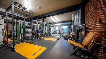 A gym with weightlifting equipment, a bench press, and a brick wall.