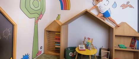Niño trepando una estructura de madera en una habitación con juguetes educativos y coloridas decoraciones en la pared.
