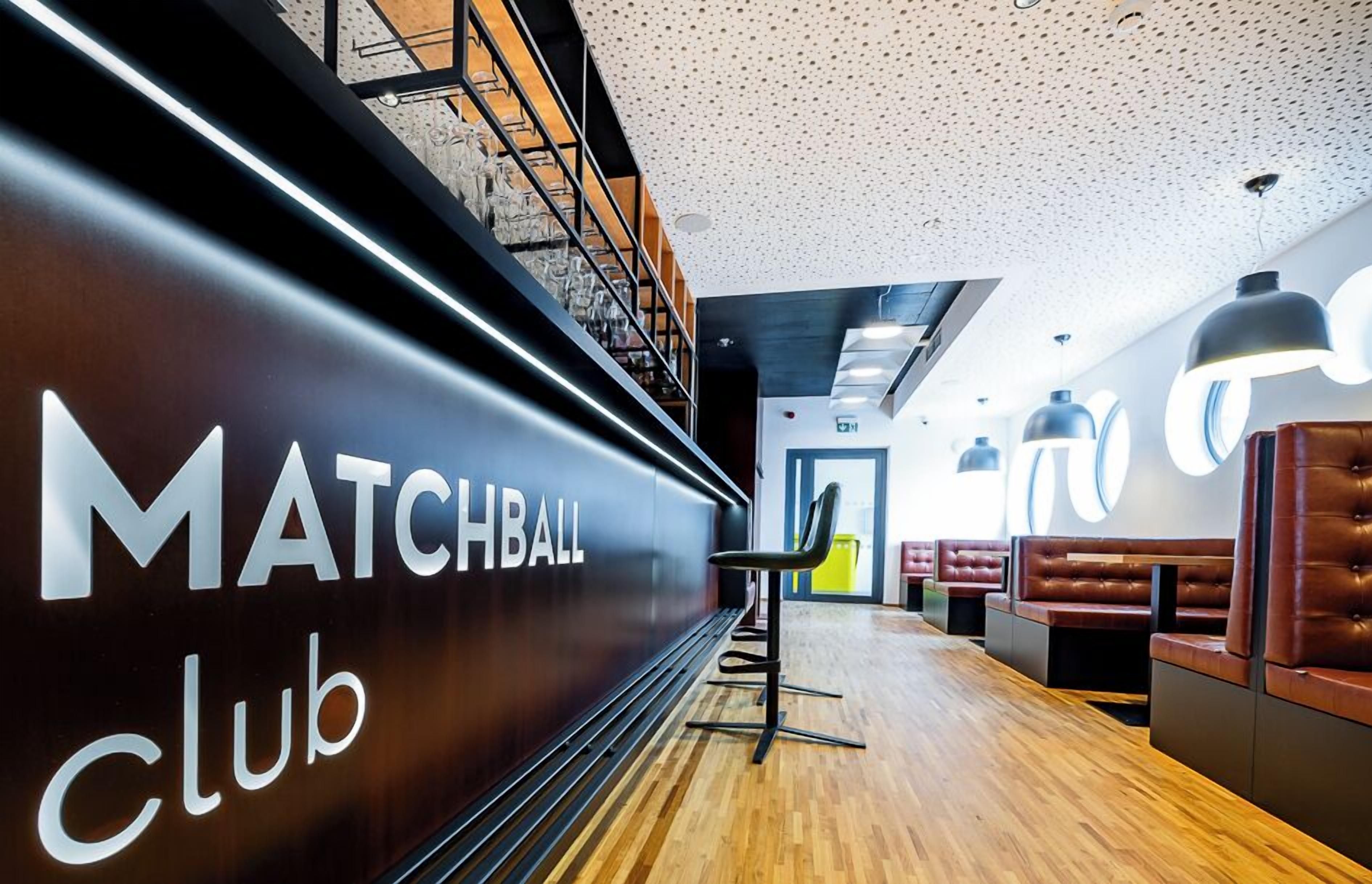 Un intérieur moderne agrémenté d'une enseigne « MATCHBALL Club », d'un plancher en bois et de coins salon.