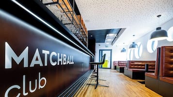 Un intérieur moderne agrémenté d'une enseigne « MATCHBALL Club », d'un plancher en bois et de coins salon.