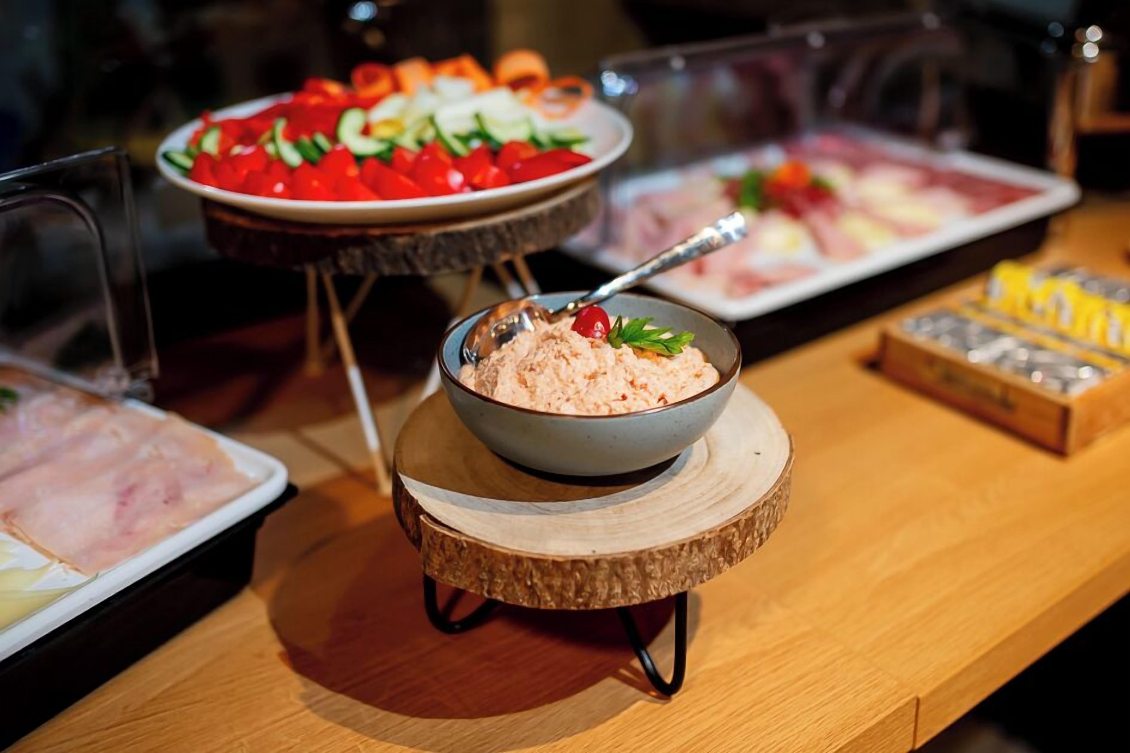 Una mesa de buffet con diversos platos, incluyendo un bol de ensalada, un plato de verduras en rodajas y una bandeja de carne.