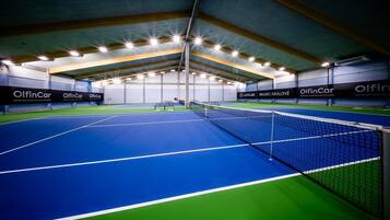 Un court de tennis intérieur, doté d’un filet et entouré de murs sur lesquels sont affichées des publicités.