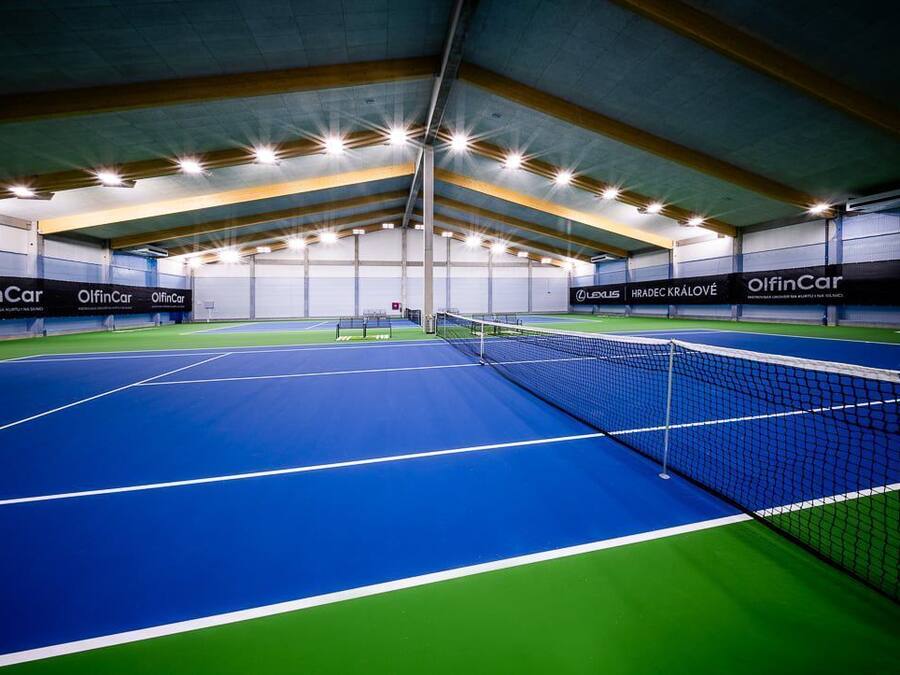 Pista coberta de tennis amb xarxa, envoltada de parets amb anuncis.