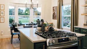 A modern kitchen with a central island, stainless steel appliances, and large windows offering a view of the outdoors. - Luxury 5BR Escape • Sleeps 10 • Patio Golf Views  • Hot Tub •  near C of I (Caldwell)