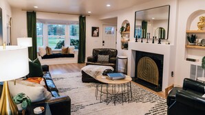 A living room with a fireplace, a sofa, a coffee table, and a view of the outdoors. - Luxury 5BR Escape • Sleeps 10 • Patio Golf Views  • Hot Tub •  near C of I (Caldwell)