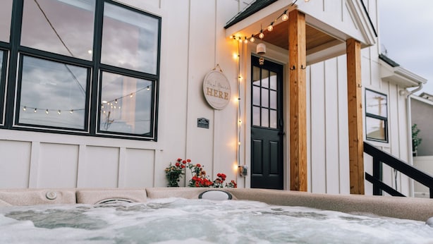 A hot tub in front of a building with a wooden porch and string lights. - Luxury 5BR Escape • Sleeps 10 • Patio Golf Views  • Hot Tub •  near C of I (Caldwell)
