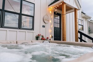 Un jacuzzi frente a un edificio con un porche de madera y luces colgantes.