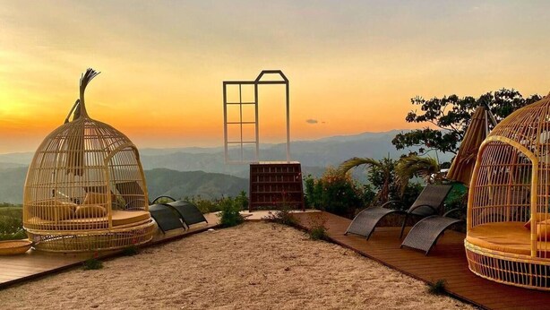 A rooftop terrace with wicker birdcages, a stone fire pit, and a view of distant mountains during sunset. - Kintiri Glamping (Belen de Nosarita)