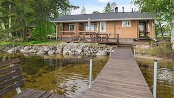 A wooden building with a dock leading to a pond, surrounded by trees.