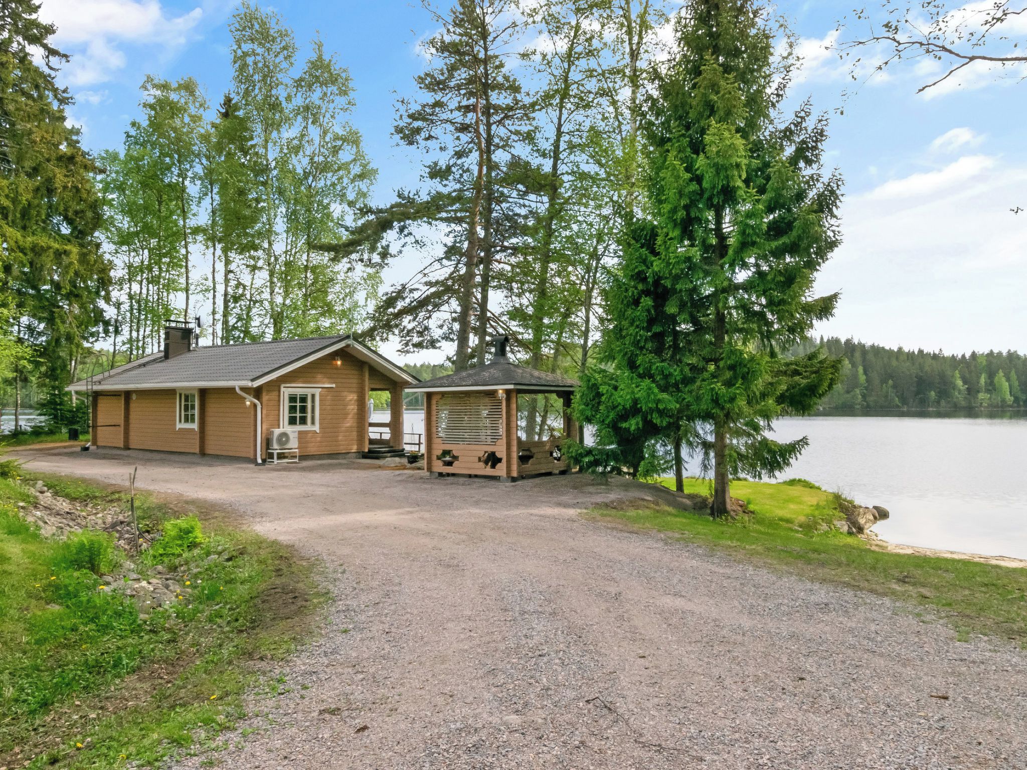 A cabin with a gravel driveway, a small porch, and a view of a lake.