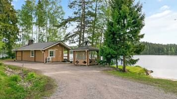 A cabin with a gravel driveway, a small porch, and a view of a lake.