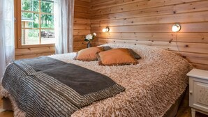 A cozy wooden cabin bedroom with a large bed, fluffy bedding, and a window with curtains. - Hiekkaranta by Interhome (Pertunmaa)