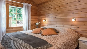 A wooden cabin bedroom with a bed, pillows, a nightstand, and a window with curtains.