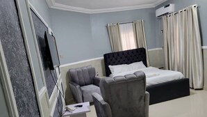 A hotel room with a bed, a grey armchair, a small table, and a TV. - international royal hotel (Owerri)