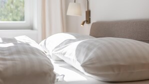 Ein ordentlich bezogenes Bett mit weißer Bettwäsche und einer Lampe an der Wand.