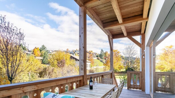 Eine Holzterrasse mit Tisch, Stühlen, einer Weinflasche und einer Decke.