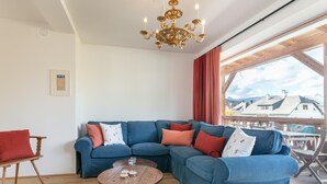 A living room with a blue sectional sofa, a wooden coffee table, and a chandelier.