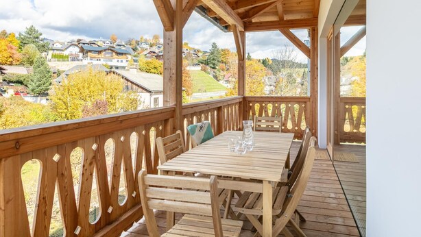 A wooden deck with a table and chairs, overlooking a residential area with autumn foliage.